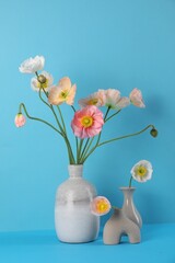 Beautiful poppy flowers in vases on light blue background, closeup