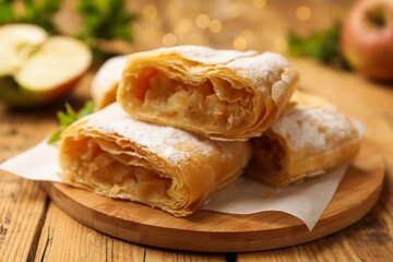 Pieces of tasty apple strudel with powdered sugar on wooden table, closeup