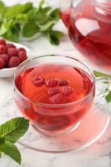 Tasty raspberry tea, berries and leaves on white marble table, closeup