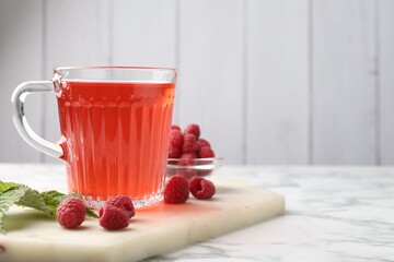 Aromatic raspberry tea in glass cup, berries and green leaves on white marble table, closeup. Space for text