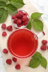 Aromatic raspberry tea in glass cup, berries and green leaves on white marble table, top view
