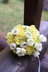 Bridal bouquet with fresh yellow and white flowers in soft lemon tones, placed on rustic wooden...