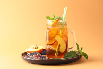 Refreshing iced peach tea with mint in mason jar on pale orange background, closeup