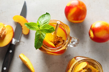 Refreshing iced peach tea with mint in mason jar and fresh fruits on light table, flat lay