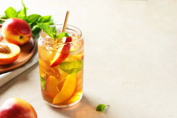 Refreshing iced peach tea with mint in glass and fresh fruits on white table, closeup. Space for text