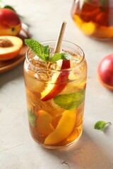 Refreshing iced peach tea with mint in glass and fresh fruits on white table, closeup