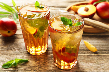 Refreshing iced peach tea in glasses and fresh fruits on wooden table, closeup