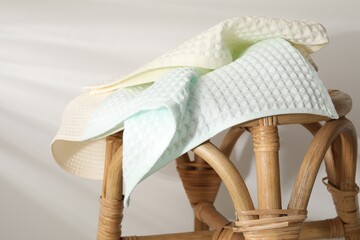Clean waffle towels on wicker chair near light wall, closeup