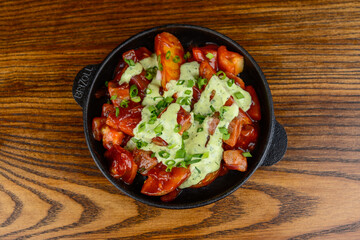 Potato fries in tomato sauce with cheese in a frying pan on a wooden background