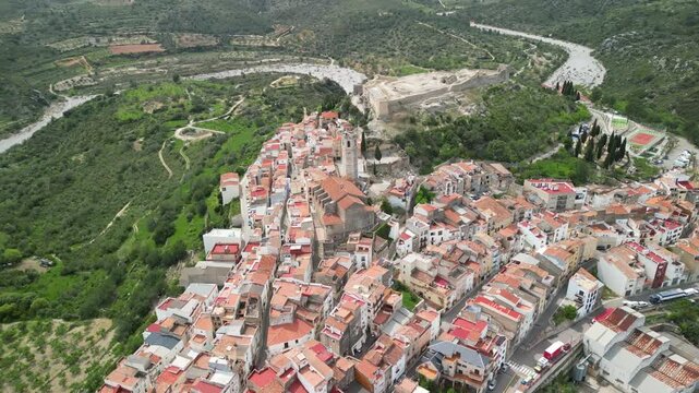 Aerial view of the ancient castle overlooking the town with terracotta rooftops nestled among the green hills, Cervera del Maestre, Valencian Community, Spain.