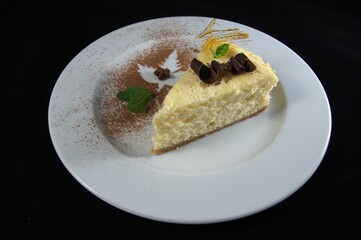 The cheesecake is decorated with chocolate shavings and mint leaves isolated on black background