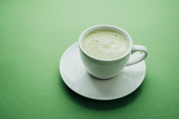 Matcha latte in white cup on green table close up