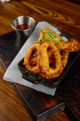 squid rings fried in batter in a pan on a wooden board with sauce macro photo