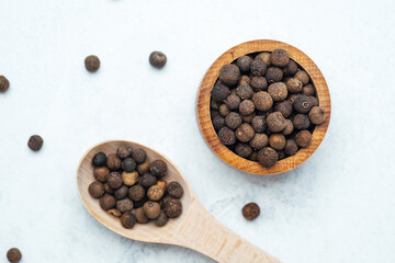 Black peppercorns in a wooden bowl and spoon on a light surface