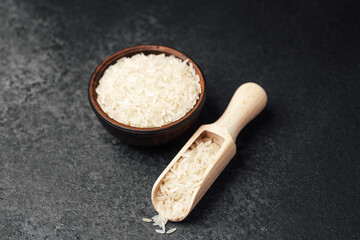 White rice in wooden bowl and scoop against dark background in kitchen