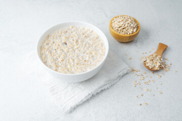 Oatmeal porridge with raw oats and wooden spoon on light background