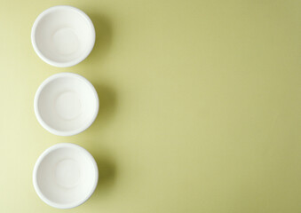 Three white ceramic bowls aligned vertically on green background