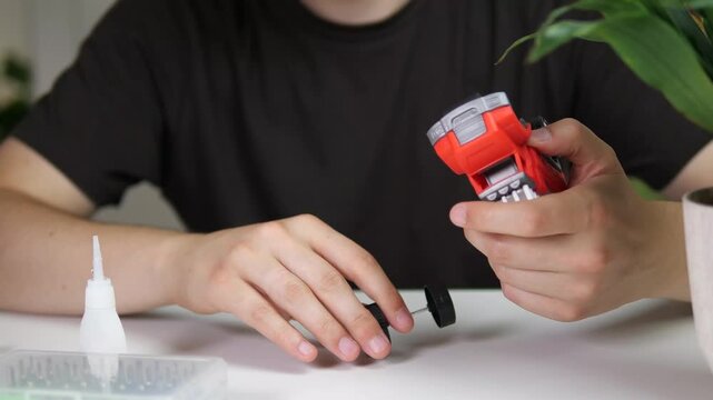  A man tries unsuccessfully to put a wheel on a children's toy car, then takes some glue and starts gluing the broken part. Fixing things.