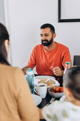 Happy family enjoying breakfast together at home. Parents and child sit at the table with fruits, eggs, toast, and drinks, sharing a warm and joyful morning moment
