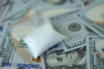 Small cocaine dose in plastic ziplock packet lies on big amount of american currency banknotes