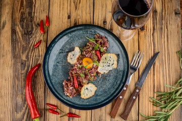 Beef tartare in a plate with croutons and pepper on a wooden background with cutlery and wine