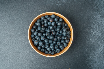 Fresh blueberries in a wooden bowl on a dark countertop