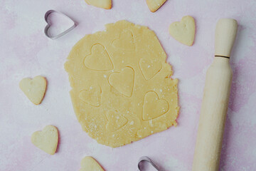 Heart shaped cookies and dough on pink background for valentine baking and love themed food concept