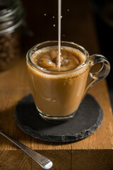 Pouring milk in a glass of coffee, hot latte drink