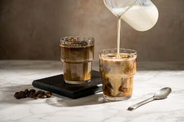 Pouring milk over glass with coffee, making iced latte coffee drink