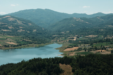 Obraz premium Beautiful aerial perspective of Rovni Lake in Serbia, with emerald water and forested shoreline. Surrounded by green hills and villages
