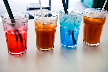 Sweet cold drinks of various flavors and colors in glasses on the table.