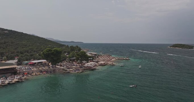 Ksamil Albania Aerial v1 low flyover bay along the shoreline, showcasing crowds on the beach and resort areas during peak summer season - Shot with Mavic 3 Pro Cine - July 18th 2024 - Powered by Adobe