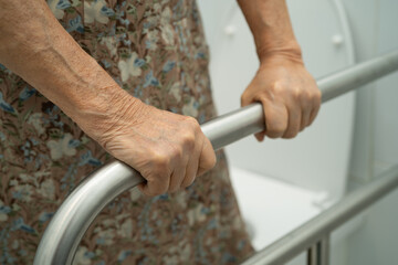 Asian elderly woman patient use toilet support rail in bathroom.