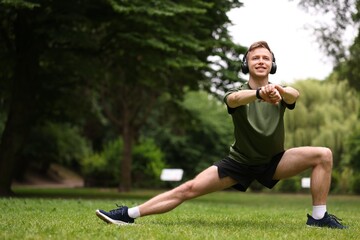 Smiling sportsman in headphones doing morning exercise in park. Space for text