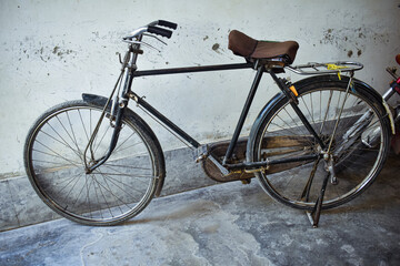 Black bicycle with brown seat parked indoors against wall for urban lifestyle and eco-friendly transport editorial