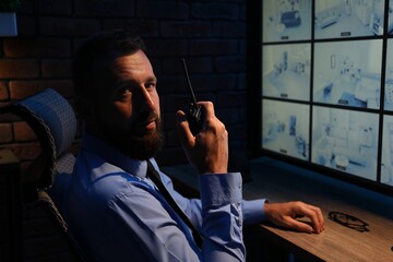 Security guard monitoring CCTV cameras and using walkie talkie in office at night