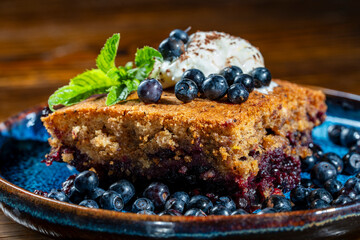 Plate with piece of fresh baked blueberry cobbler and ice cream on wooden background, closeup. Homemade berry cobbler ready to eat