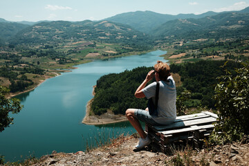 Woman sitting above Rovni Lake in Serbia, admiring the panoramic mountain scenery. Side view....