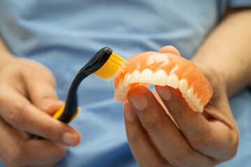 Asian senior woman patient clean teeth denture with toothbrush for chew food.