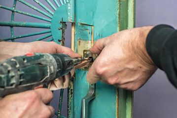 Closeup of male workers drilling the hole in old door to replace the lock. Repairing metal door,...