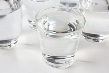Clear drinking water in various glass cups arranged on a white surface.