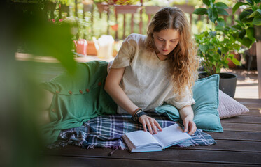 Beautiful young woman reading a book lying on a summer terrace of a country house