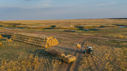 A tractor on a farm is stacking hay bales from a cart into a stack