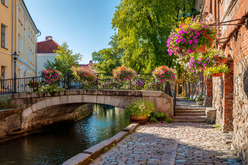 Elegant stone bridge with flower baskets over a canal in a small European town, cobblestone walkway 
