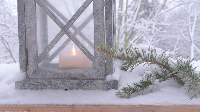 Christmas tree decoration, soft flame first Advent candle flickers inside garden lantern with snow gently falling in background for wintery feel, cozy Christmas scene