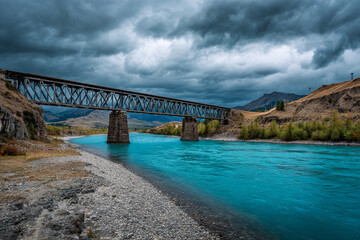 Old railway bridge crossing a turquoise mountain river, dramatic clouds overhead