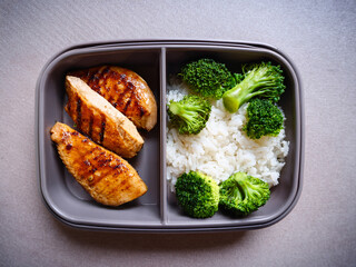 Healthy lunch box with grilled chicken, brown rice, and steamed broccoli &ndash; flat lay