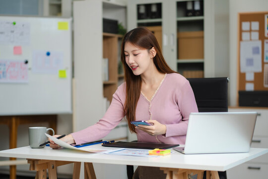 Female coder or developer working using a computer display and smartphone in problem solving at workplace.