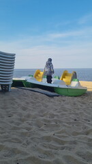 Stack of sun loungers on the beach.  Start or end of the summer season at the resort city. Heap of sunbeds at the coastline. Boy stands on a catamaran.