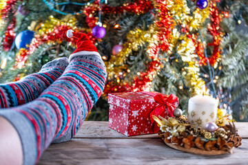 pair feet wearing colorful Christmas socks, resting near decorated Christmas tree, cozy winter...